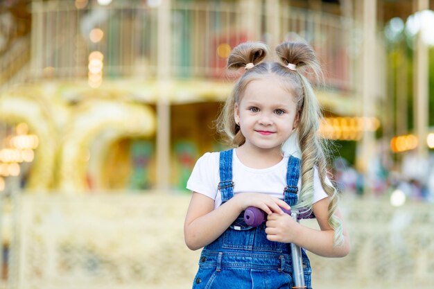 Une fille joyeuse dans un parc d'attractions sur le fond d'un carrousel monte un scooter