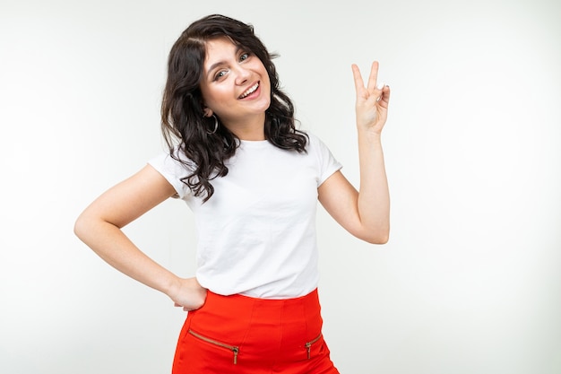 Fille joyeuse dans un T-shirt blanc montre deux doigts sur un fond blanc.