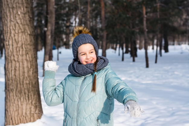 Une fille joyeuse dans des vêtements chauds lance une boule de neige dans un parc d'hiver