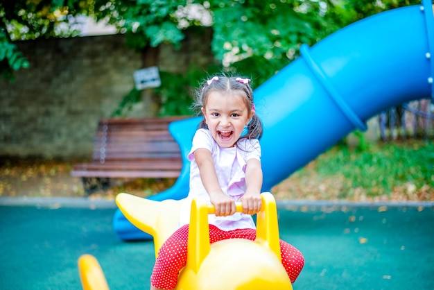 Une fille joyeuse avec deux nattes sur la tête monte une balançoire dans le parc et rit