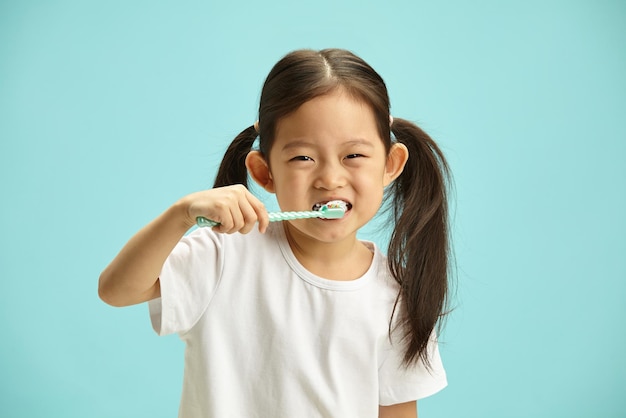 fille joyeuse enfant avec se brosser les dents en prenant soin de l'hygiène dentaire debout sur bue isolé