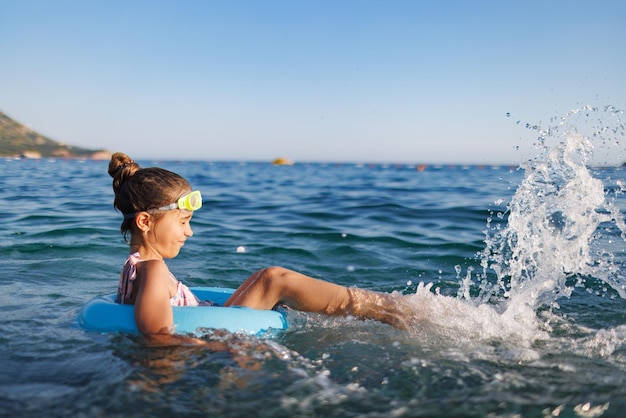 Une fille joyeuse est assise dans un cercle gonflable et éclabousse d'eau dans la mer