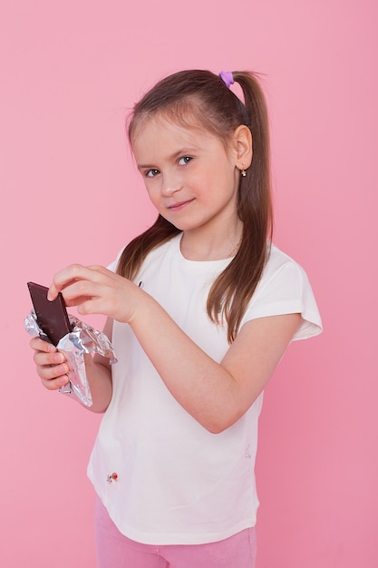 Fille joyeuse à moitié nue au gingembre souriant et mangeant du chocolat isolé sur un mur rose.