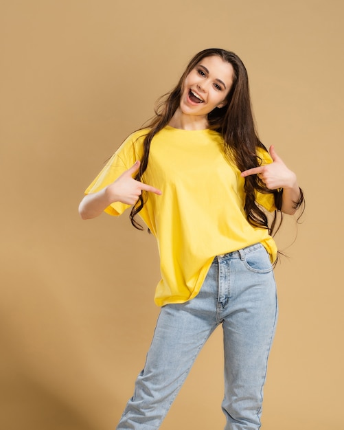 Photo une fille joyeuse montre avec ses doigts un t-shirt jaune porté sur son corps.