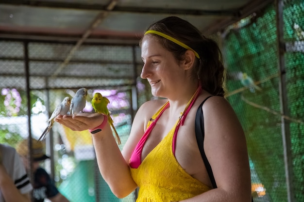 une fille joyeuse nourrit les perroquets de ses mains et rit. contacter le zoo.