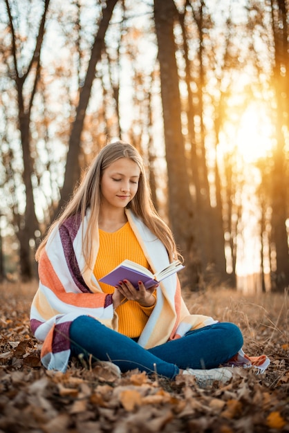 fille joyeuse portant un pull orange recouvert de plaid chaud dans le parc en automne