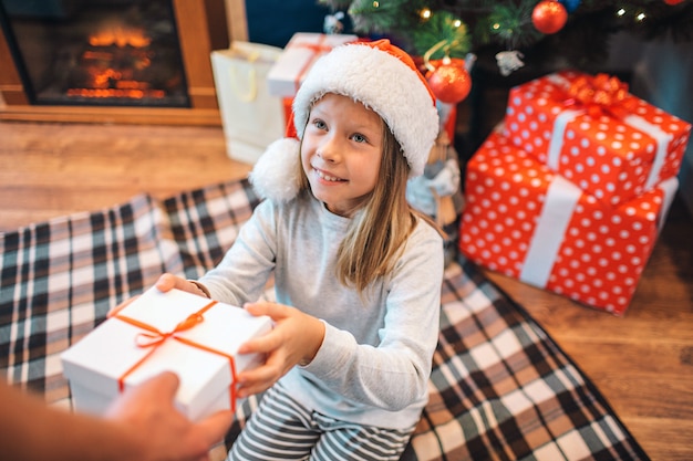 Une fille joyeuse prend une boîte avec un cadeau et regarde un adulte qui le lui donne.