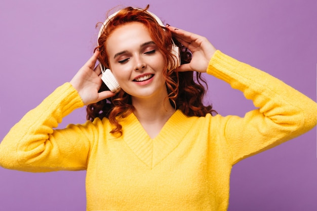 Une fille joyeuse en pull jaune et casque écoute des chansons avec le sourire