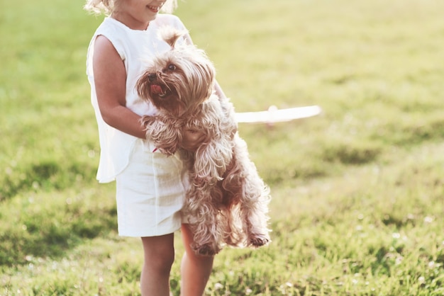 Fille joyeuse souriante tenant un petit chien et jouant avec lui à l'extérieur sur le terrain