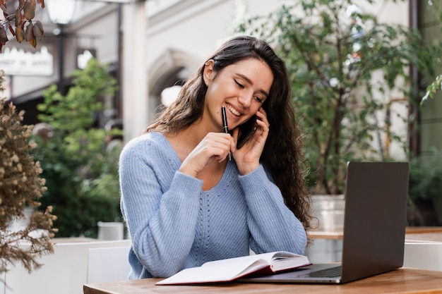 Une fille joyeuse avec un téléphone et un ordinateur portable travaille en ligne avec des clients et discute avec l'équipe Une femme d'affaires occupée avec un ordinateur portable et un téléphone discute et travaille à distance avec des collègues