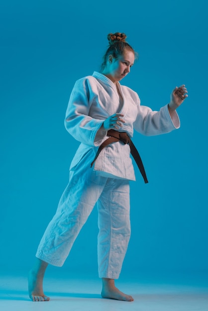 une fille judoka dans un kimano blanc avec une ceinture noire sur un fond bleu photo de studio
