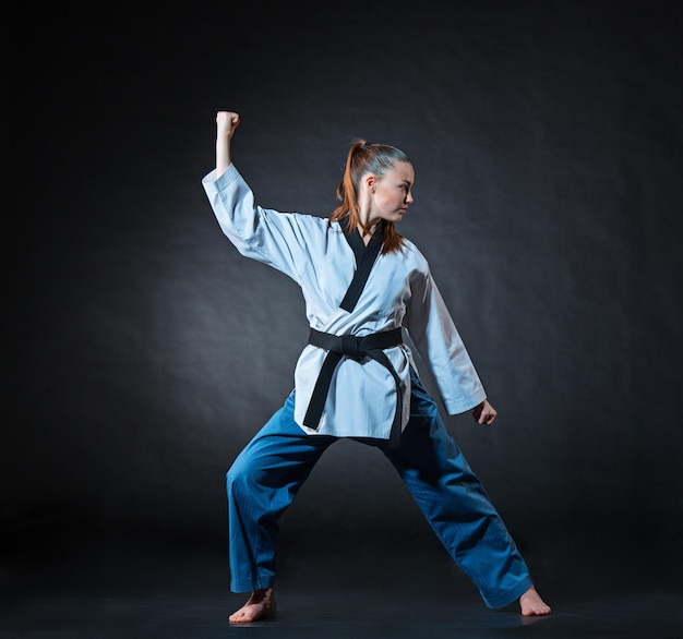 La fille de karaté en kimono blanc et karaté d'entraînement de ceinture noire sur fond gris.