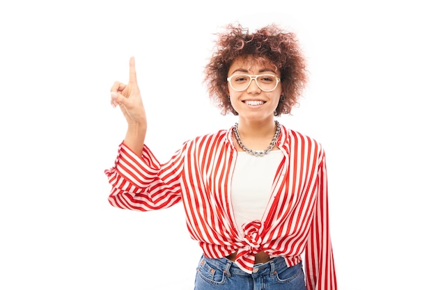 Fille kazakhe positive avec une coiffure afro pointe l'index à l'espace de copie isolé sur fond de studio blanc