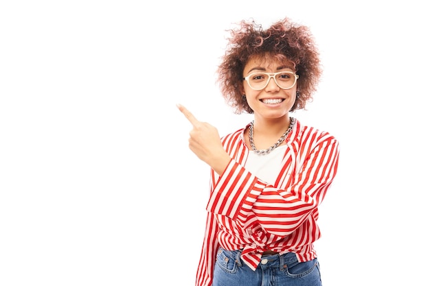 Fille kazakhe positive avec une coiffure afro pointe l'index à l'espace de copie isolé sur fond de studio blanc