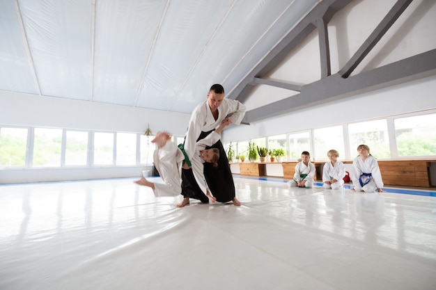 Fille de lancer. Entraîneur d'aïkido jetant une fille en kimono blanc tout en lui apprenant à se protéger