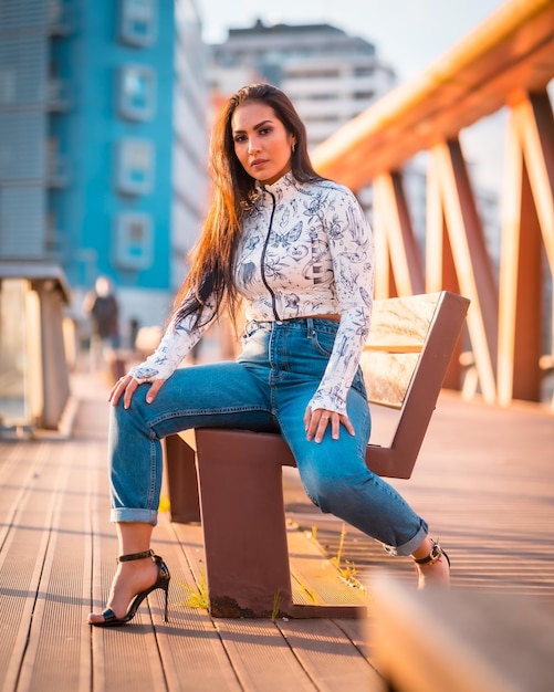 Une fille latine brune en jeans dans la ville au coucher du soleil Sur un pont en regardant la rivière de la ville