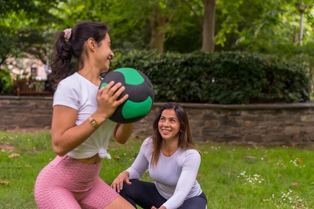 Fille latine faisant du sport dans un parc verdoyant, mode de vie une vie saine, professeur attentif avec les étudiants dans l'exercice de squats avec le ballon de musculation