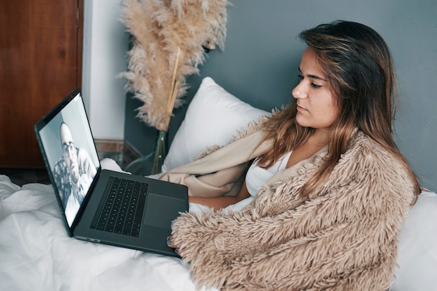 Une fille latine malade au lit passe un appel vidéo avec un ordinateur portable à son médecin