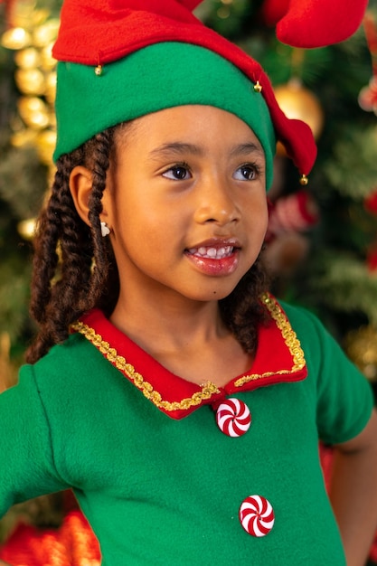 Fille latino-colombienne afro-colombienne de 5 ans habillée en elfe à côté de l'arbre de Noël