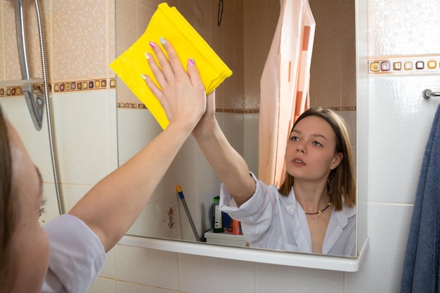 La fille lave le miroir dans le concept de nettoyage de salle de bains