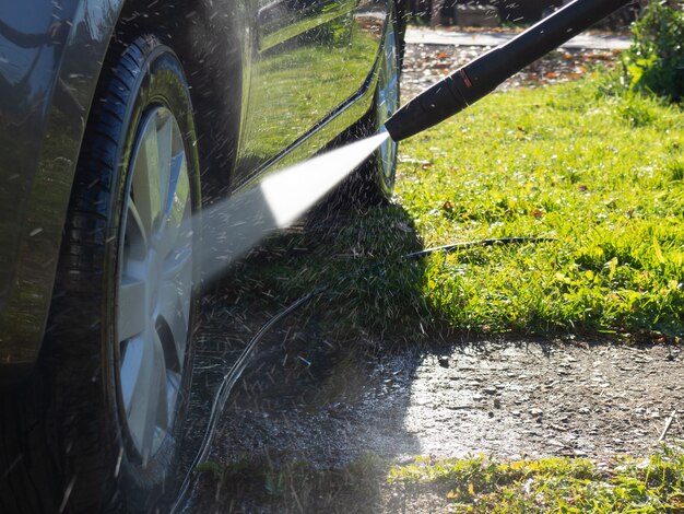 La fille lave la voiture à la maison près du garage à l'aide d'un nettoyeur haute pression