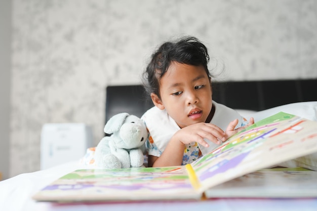 Une fille lit un livre avec un animal en peluche dessus.