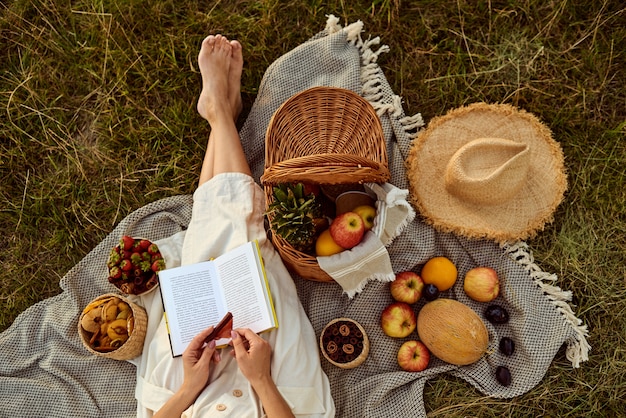 Fille avec un livre dans ses mains se détendre lors d'un pique-nique en plein air sur une journée ensoleillée. Vue de dessus.