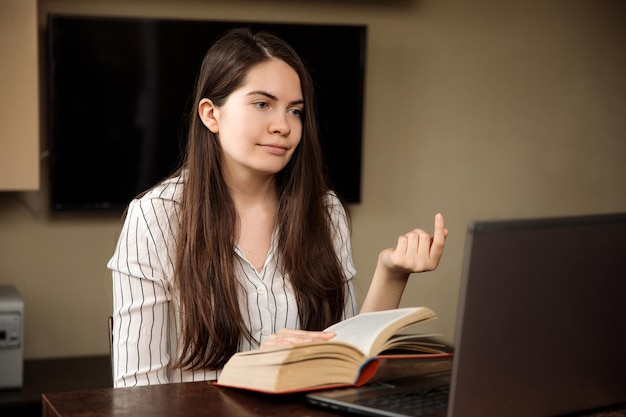 Une fille avec un livre explique quelque chose enseigne par liaison vidéo devant un ordinateur portable