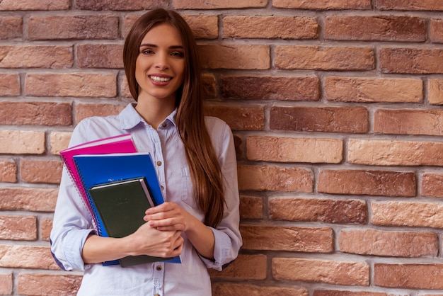 Fille avec des livres se trouve près du mur de briques.