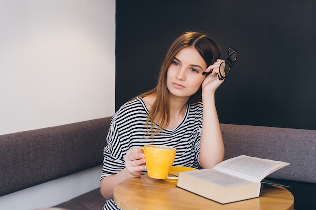 Fille à lunettes en lisant un livre dans un café