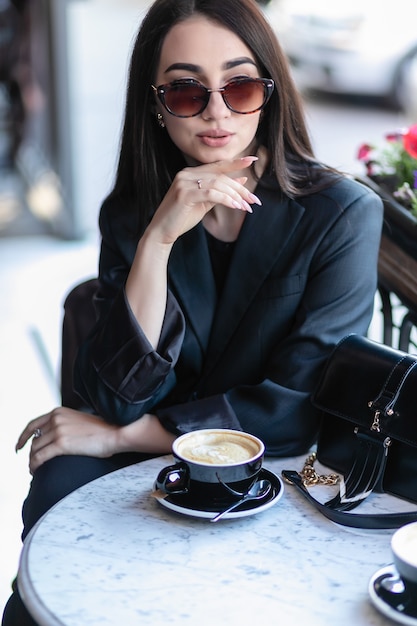 Fille avec des lunettes de soleil assise dans un café, un café, assise sur une chaise dans la ville avec des fleurs rouges, portant des lunettes de soleil