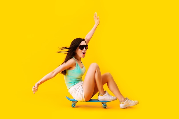 Fille à lunettes de soleil, assise sur une planche à roulettes, sur un espace jaune