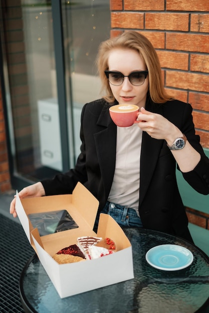 Fille à lunettes de soleil dans un café de rue avec boîte-cadeau