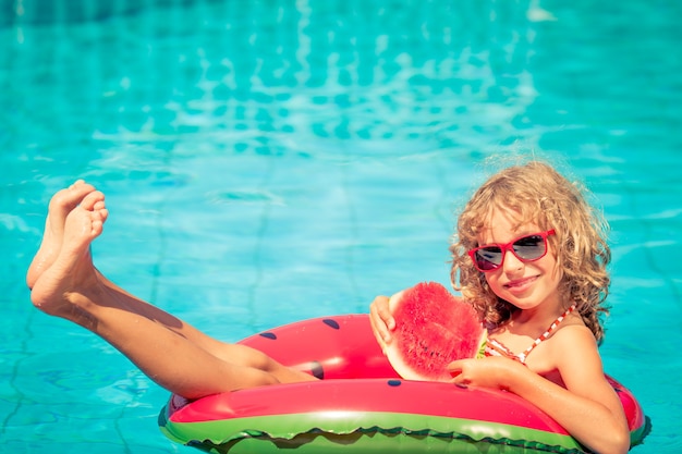 Fille avec des lunettes de soleil rouges tenant une pastèque sur une pastèque gonflable dans la piscine