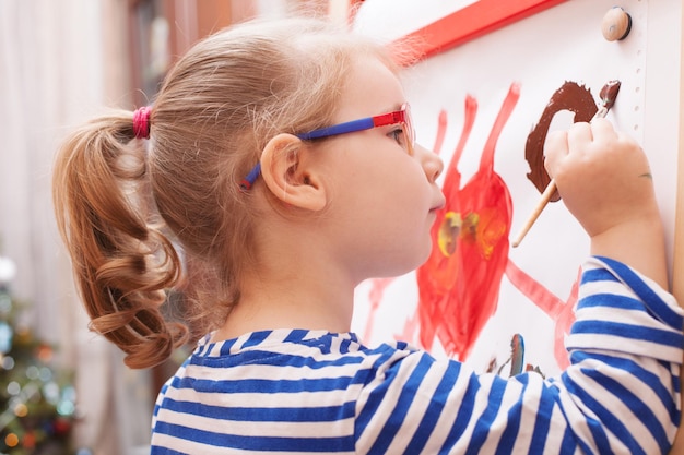 Fille avec des lunettes et un t-shirt rayé peint des peintures sur toile blanche