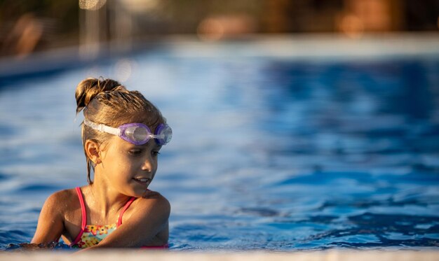 Une fille en maillot de bain brillant avec des lunettes de natation plonge dans une piscine à l'eau claire et transparente