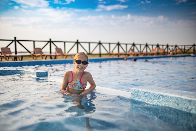 Une fille en maillot de bain brillant et lunettes de natation pose près de la piscine en train de bronzer sous le soleil d'été