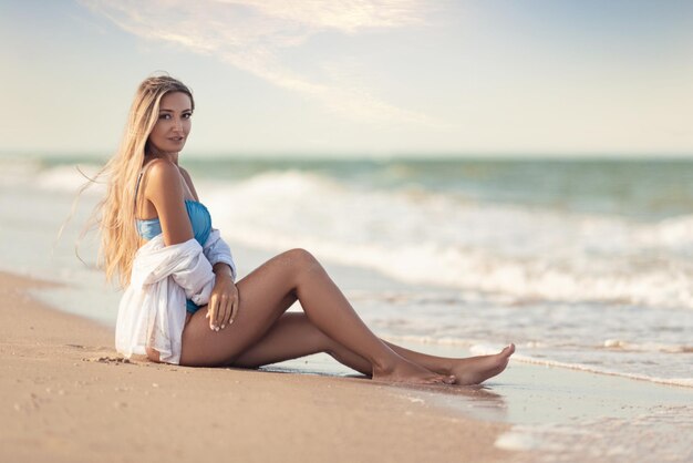 Une fille en maillot de bain et chemise bleuâtre est assise près du bord de l'eau et regarde à l'horizon