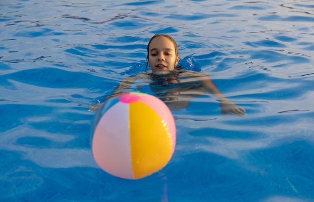 Une fille en maillot de bain lumineux nage avec un ballon gonflable dans une piscine à l'eau claire un soir d'été