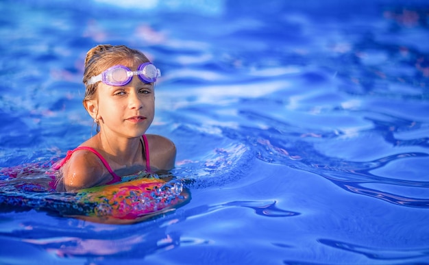 Une fille en maillot de bain lumineux nage avec un ballon gonflable dans une piscine à l'eau claire un soir d'été