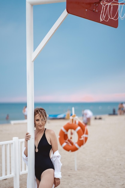 une fille en maillot de bain noir et une chemise blanche sur un terrain de basket sur la plage