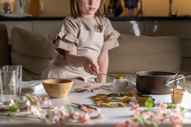 Une fille à la maison dans la cuisine teint des œufs pour Pâques