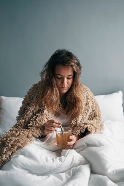 Une fille malade au lit avec une couverture boit du thé chaud