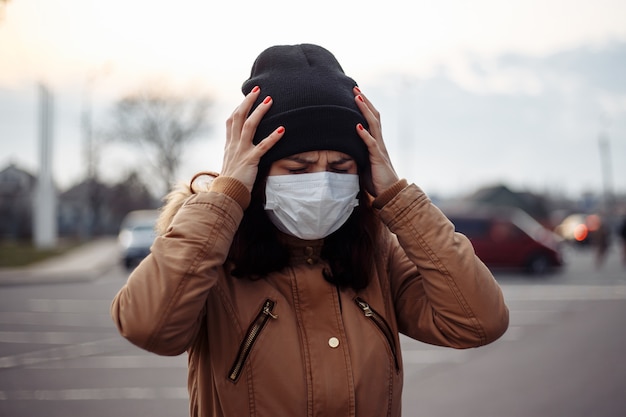 Une fille malade malade porte un masque médical femme anxieuse dans un masque souffrant de chaleur, des maux de tête se débat dans la rue, se sentant mal. La personne a besoin d'aide. Virus, coronavirus pandémique chinois, concept de panique.