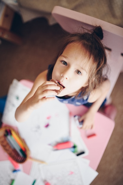 Photo une fille mange un cookie tout en étant assise à une table.