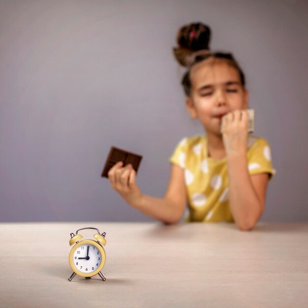 Fille mangeant des barres de chocolat avec plaisir et sans tenir compte de l'horloge devant elle