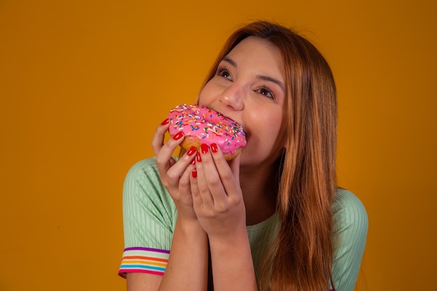 Fille mangeant des beignets roses sur fond jaune.