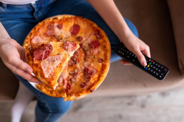 Fille mangeant de la pizza assise sur un canapé et regardant la télévision dans un appartement moderne