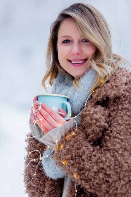 fille en manteau avec une tasse de boisson dans une forêt de neige