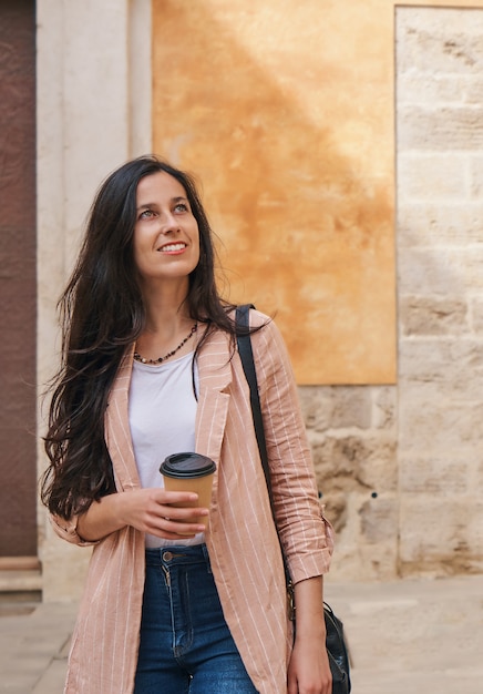 Fille marchant dans une vieille ville en vacances avec une tasse de café